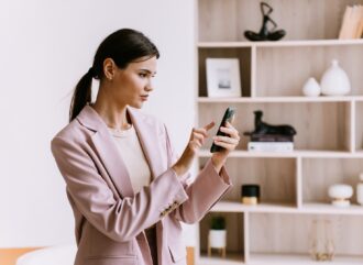 Focused professional woman in pink blazer using smartphone in modern office, embodying efficiency an